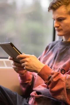 Smiling young man reading e-book when he traveling by train. Man sits at the Stock Photos