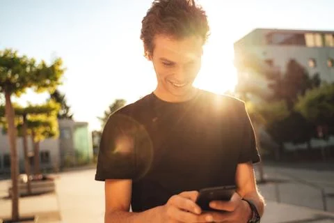 Smiling young man reading text message on smartphone in city on sunny day Stock Photos