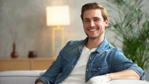 Smiling young man relaxing on couch, resting at home and looking at camera Stock Footage 186456614