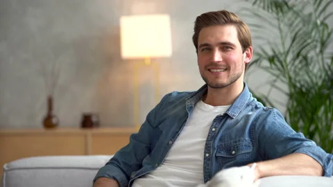 Smiling young man relaxing on couch, resting at home and looking at camera Stock Footage 186459853
