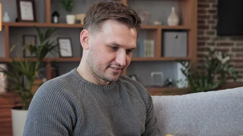 Smiling young man sitting on couch using laptop typing message online. Stock Footage 172394344