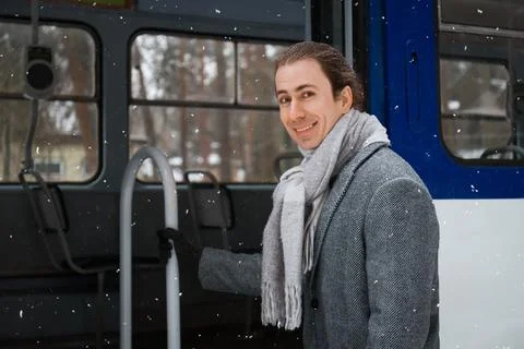 Smiling young man standing in the open doorway of a tram during a snowfall... Stock Photos