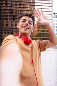 Smiling young man taking a selfie waving hand outdoors in the city Foto stock