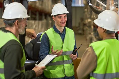 Smiling young man talking to group of workers in warehouse Stock Photos