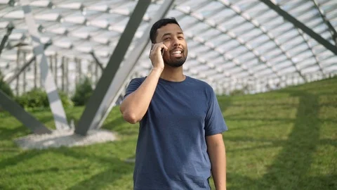 Smiling young man talking on phone standing on green lawn Vídeo Stock 97201186