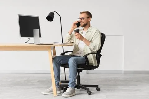 Smiling young man talking on smartphone and drinking coffee at modern home of Stock Photos