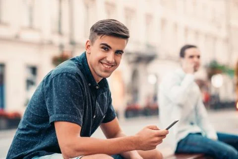 Smiling young man texting on a bench in the city Stock Photos