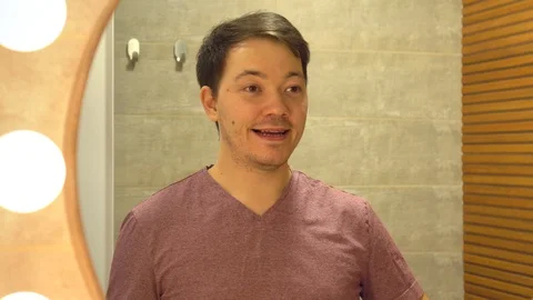 A smiling young man with a toothbrush brushing his teeth and looking at the Stock Footage 128774649