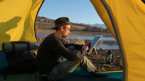 Smiling young man tourist using smartphone sitting in touristic tent at the Видео 75789759