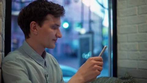 Smiling young man typing messages on smartphone in cafe in the evening Stock Footage 77168787