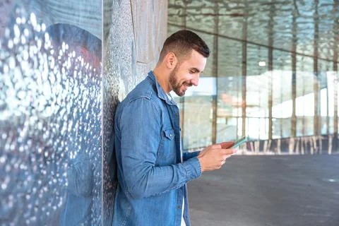 Smiling young man using an app on his smartphone and standing outdoors. Stock Photos