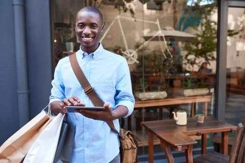 Smiling young man using a digital tablet while out shopping Stock Photos