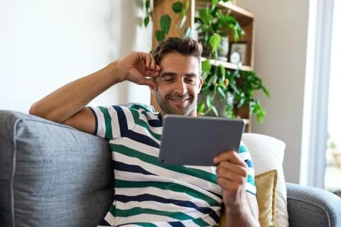 Smiling young man using a digital tablet on his sofa Stock Photos