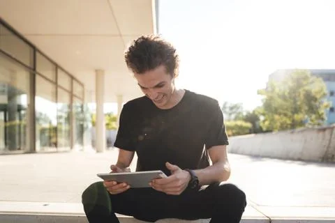 Smiling young man using digital tablet while sitting outside university Stock Photos