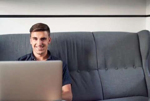 Smiling young man using a laptop at home Stock Photos
