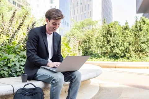 Smiling young man using laptop sitting on a bench Stock Photos