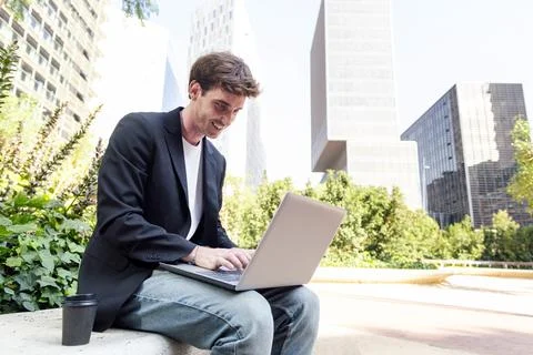 Smiling young man using laptop sitting on a bench Foto stock