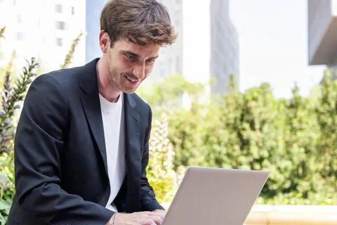 Smiling young man using laptop sitting on a bench Stock Photos