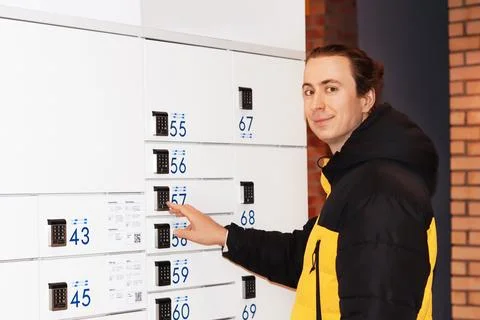 Smiling young man using a self-service parcel locker terminal to pick up a .. Stock Photos