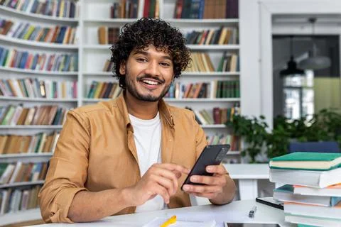 Smiling young man using smartphone at a study desk 写真素材