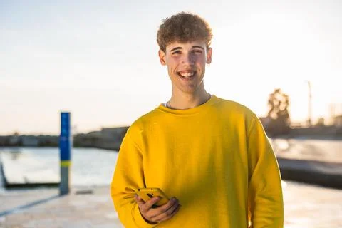 Smiling young man using smartphone at sunset in urban setting Stock Photos