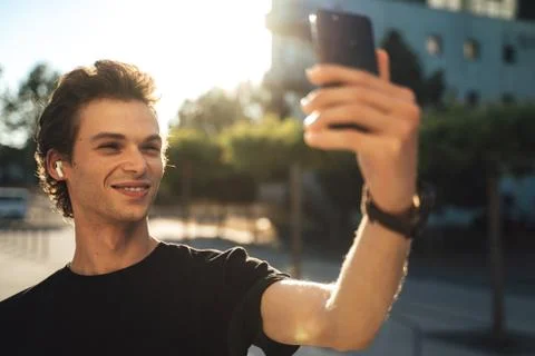 Smiling young man using video chat on mobile phone at college campus Stock Photos