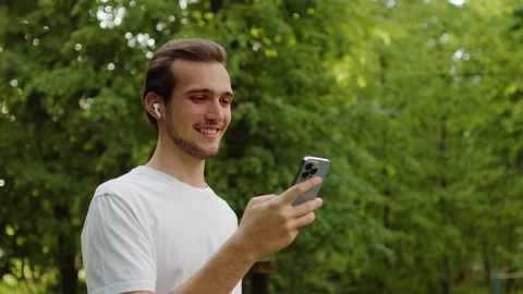 Smiling young man on a video call wearing headphones, in a green park. Stock Footage 335206732