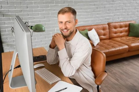 Smiling young man working at computer desk in modern home office 스톡 사진