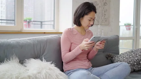 Smiling young mixed race asian girl holding credit card and smartphone sitting Stock Footage 142134717