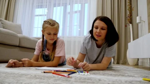 Smiling young mom and cute preteen daughter lying on warm floor at home drawing Stock Footage 134853014