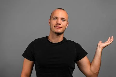 Smiling young presenting something in his palm against a gray background. Stock Photos