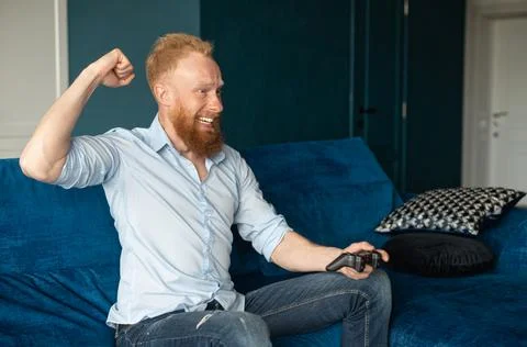 Smiling young redhead man win in video game and feel happy Stock Photos