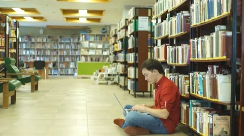 Smiling young student sitting on library floor using laptop in college Stock Footage 68577641