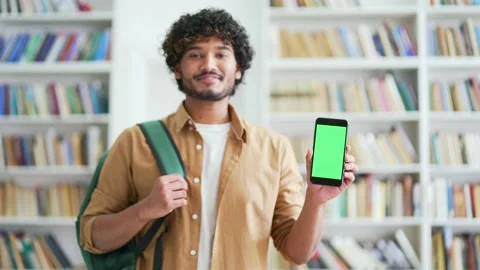Smiling young university student showing smartphone with green screen while  Stock Footage 239735168