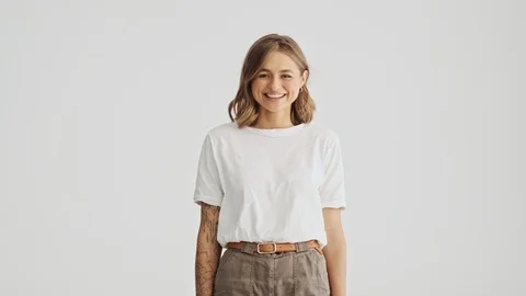 Smiling young woman in basic t-shirt raises hands up isolated over white wall Stock Footage 120071494
