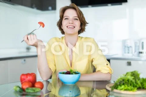Smiling young woman eating fresh salad in modern kitchen Stock Photos