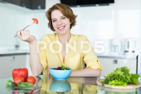 Smiling young woman eating fresh salad in modern kitchen Stock Photos