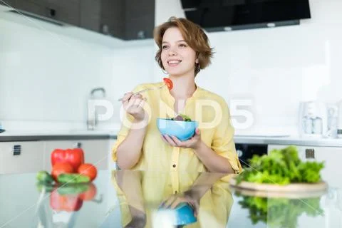 Smiling young woman eating fresh salad in modern kitchen Stock Photos
