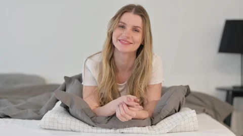 Smiling Young Woman Looking at Camera while Lying on Stomach in Bed Video stock 299754366