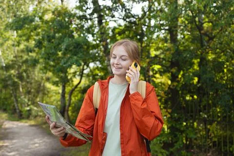 Smiling young woman with map talking on smartphone during forest hike Stock Photos