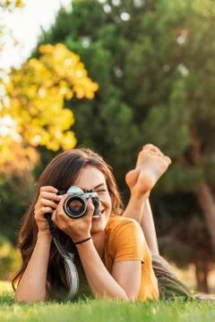 Smiling young woman using a camera to take photo at the park. Stock Photos