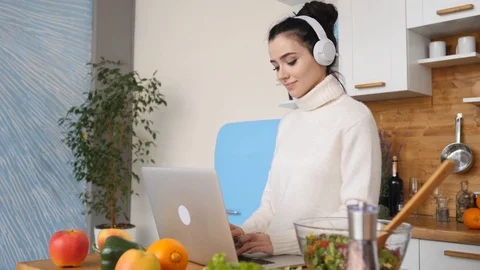 Smiling Young Woman Using Laptop In Kitchen Wearing Headphones At Home Видео 105301104