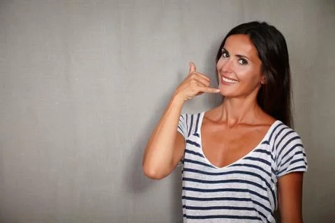 Smiling youngster gesturing a call while standing against grey texture backgr Stock Photos