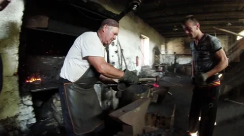 Smith and His Apprentice Handles Iron Piece in the Forge in the Carpathians Stock Footage 59761325