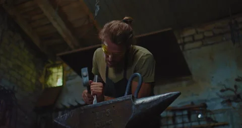 Smith is using chisel for decorating forged item in workshop, work on anvil, 4K Stock-Footage 205161271