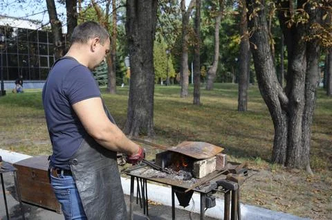 At the smithy workshop. Blacksmith holds forceps with a metal billet in a Stock Photos