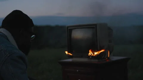 Smoke and fire erupt from old TV in remote field at sunset Stock Footage 319969320