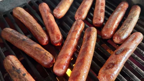 Smoke and flames rises slowly from grilled hot dogs Stockbeeldmateriaal 337577635