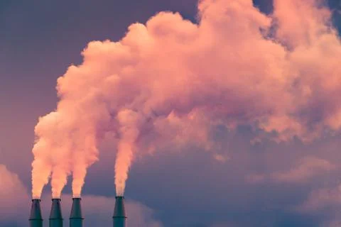 Smoke and steam rising into the air from power plant stacks; dark clouds back Stock Photos