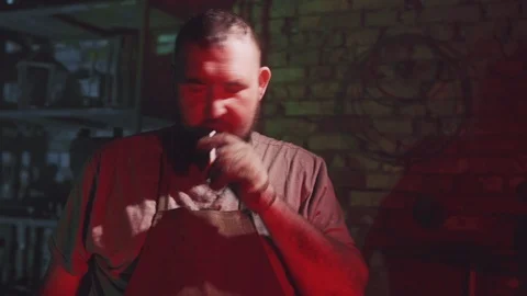 Smoke break of a bearded blacksmith at a workplace in his forge Stock Footage 108032760